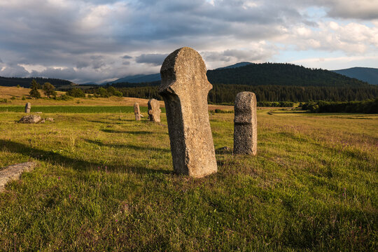 Medieval stecci tombstones at Maculje in Bosnia and Herzegovina, standing in a mountain meadow with forested hills and dramatic evening clouds