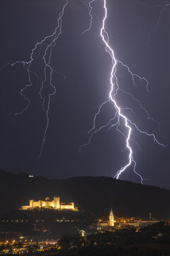 View of a powerful lightning strike illuminating the night sky over the historic Rocca Albornoziana fortress and the town of Spoleto, Umbria, Italy.