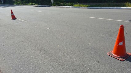 Bright orange traffic cones placed on gray asphalt road surface area © Sueliton