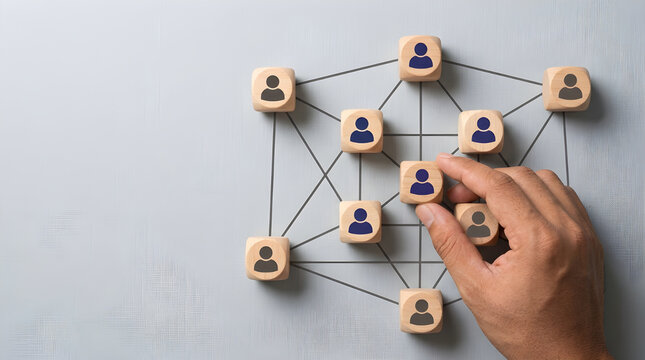 Wooden cubes with human icons arranged in a network structure managed by a human hand closeup