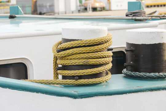 Yellow rope wraps boat bollard. Thick mooring line circles metal post. White paint covers bollard top. Turquoise deck surrounds equipment. Second post appears in background. Boat hardware in closeup.