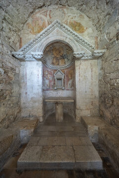 View of the ancient stone altar and faded frescoes inside the historic Temple of Clitunno in Pissignano, Umbria, Italy.