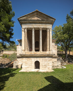 View of the ancient Temple of Clitunno with its stone facade and Corinthian columns set in a lush garden in Pissignano, Umbria, Italy.