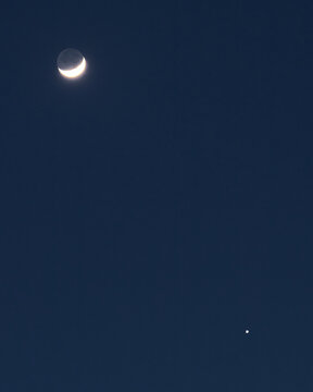 View of a crescent moon and a bright planet in the dark night sky above Roma, Lazio, Italy.