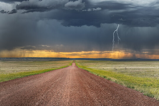 A remote road in the arid great plains framed by a large storm signifies the remote and harsh climate of the region 