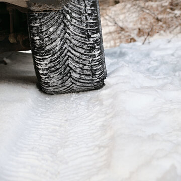 Close-up of a car winter tire with snow in the tread, showing traction pattern on a snowy road during cold weather conditions