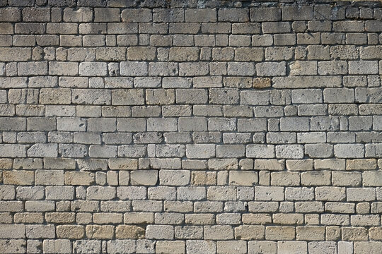 Close-up of an aged gray brick wall with rough stone texture, irregular blocks and weathered surfaces. Rustic masonry background with a timeless architectural character