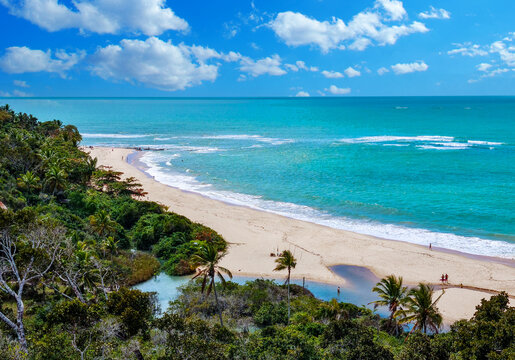 Stunning panoramic view of Praia de Pitinga in Arraial d'Ajuda, Bahia, Brazil. Tropical beach featuring turquoise waters, white sand, and lush vegetation under a blue sky.