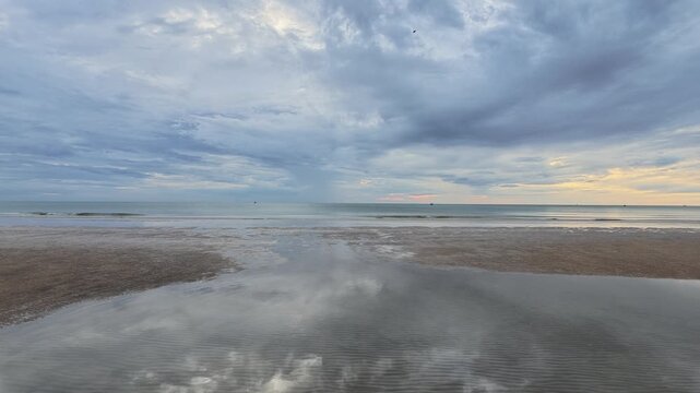 Dramatic clouds reflecting on wet sand at low tide beach at sunrise