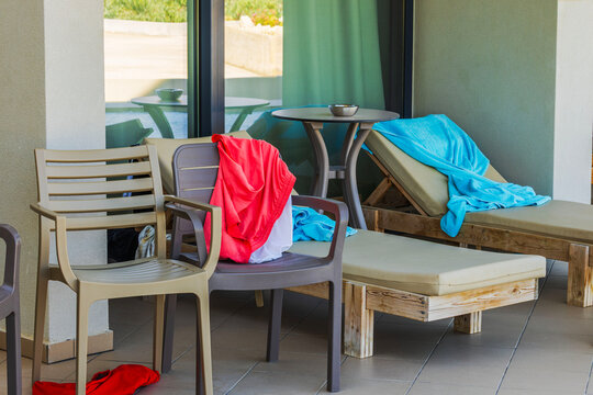 Close-up view of hotel terrace with sun loungers, chairs, table, towels and swimwear. Crete. Greece.