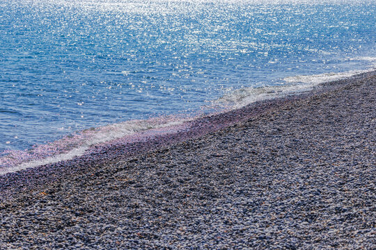 Beautiful view of gentle sea waves washing pebble beach with sunlight sparkling on water. Crete. Greece.