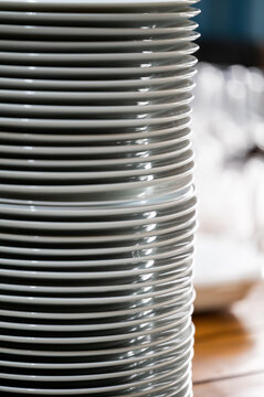 A tall stack of clean white ceramic plates on a wooden table, close-up view
