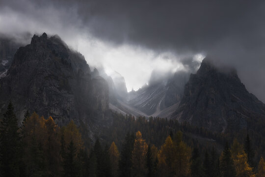 View of the dramatic rocky peaks of Tre Cime di Lavaredo rising above the autumn larch forest near Lake Antorno in Auronzo di Cadore, Veneto, Italy.