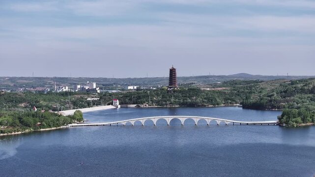 Scenic lake view with arched bridge and distant pagoda surrounded by hills and forests
