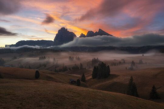 View of Alpe di Siusi at sunrise with dramatic mist rolling over the alpine meadows and the jagged peaks of the Dolomites in Bolzano, Trentino-Alto Adige, Italy.