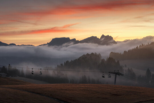 View of Alpe di Siusi with a chairlift silhouetted against a misty mountain landscape during a golden sunset in Bolzano, Trentino-Alto Adige, Italy.