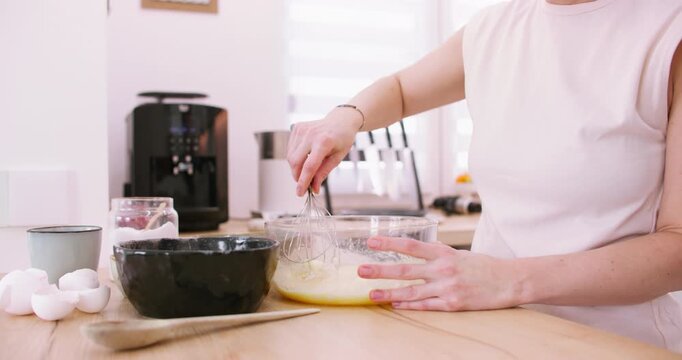 Baker occupation. Mixing meal. Female hand stirring liquid dough with whisk at light home kitchen modern workplace preparing dessert.