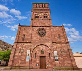 Fototapeta premium Exterior view of Saint Thomas Church in Strasbourg, France, featuring its monumental red sandstone facade, Gothic architectural elements, large rose window, and prominent square clock tower.