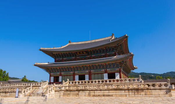 Majestic historic Korean palace building with intricate architecture and stone platform under a clear blue sky