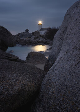 View of Phare de Pontusval illuminated at dusk, surrounded by large granite boulders on the coast of Plouneour-Brignogan-plages, Bretagne, France.