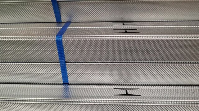 Galvanized metal profiles lie stacked together with blue plastic straps in a hardware store. construction materials, building supply, hardware store warehouse.
