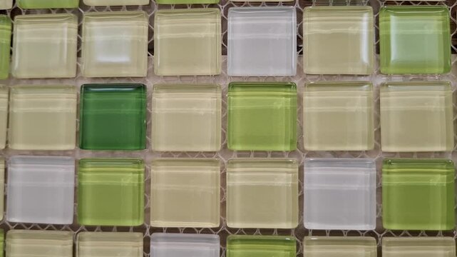 Green and white glass mosaic tiles lie stacked on a mesh backing in a store. construction materials, interior design renovation, bathroom wall cladding.