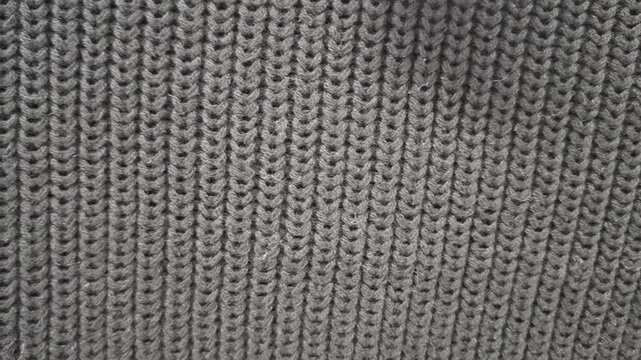 Close view of gray knitted fabric with a repeating woven pattern, soft textile surface, cozy material, clothing production, and interior texture.