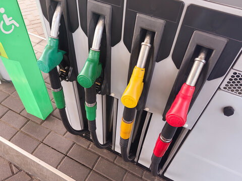 Fuel dispenser with four nozzles in green, yellow, red, and black colors at a gas station, featuring a wheelchair accessibility symbol on the side