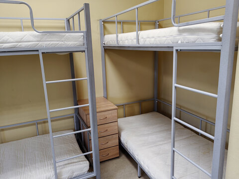 Bunk beds with metal frames and mattresses in a shared room, wooden dresser positioned between the beds against a yellow wall in a dormitory setting