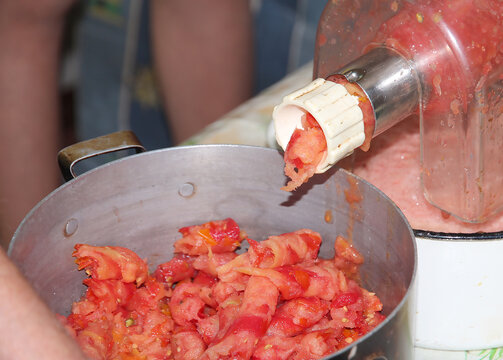 Traditional homemade tomato processing with a manual grinder, turning fresh ripe tomatoes into smooth pulp for sauce, puree, and food preservation in a home kitchen.