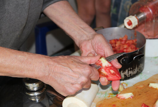 Close-up of men's hands cutting a fresh tomato, preparing homemade tomato sauce in an electric meat grinder among pieces of juicy tomatoes