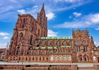 Fototapeta premium Wide view of Strasbourg Cathedral showing its Gothic facade, monumental tower, ornate tracery, stained glass windows, sandstone walls and green copper roofs in Strasbourg, France.