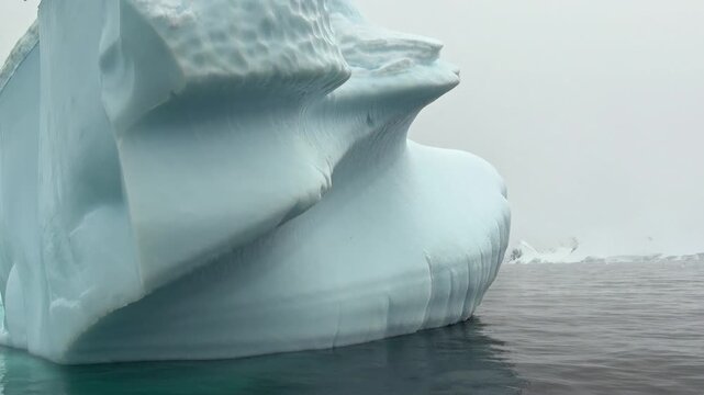 Ancient glaciers drift across Antarctica's dark, misty waters, showcasing breathtaking, naturally sculpted shapes carved over centuries in this remote, frozen wilderness.