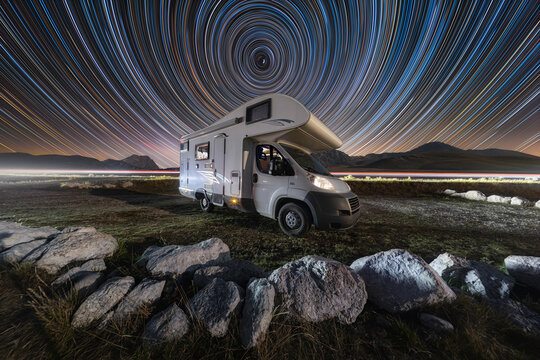 View of a camper van parked under a vibrant star trail sky at Campo Imperatore L'Aquila, Abruzzo, Italy.