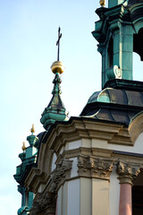 Close-up of ornate green copper domes and spires topped with a christian cross on St. Nicholas Church in Prague, Czech Republic. Baroque architectural detail. © VladyslavShcherbakov