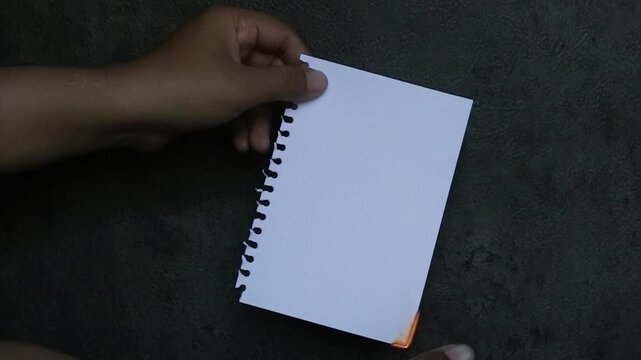An Asian hand holds a sheet of paper about to be set on fire with a lighter, against a black background.