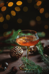 Naklejka premium Festive still life featuring a glass of sparkling rose wine, evergreen branches and Christmas ornaments on a dark table with warm seasonal atmosphere and copy space