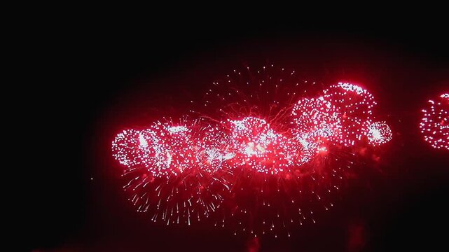 Brilliant red fireworks explode in the night sky. Bright bursts of color punctuate the darkness as sparks fall, creating a stunning summertime celebration.