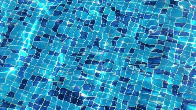 Clear turquoise pool water flows over blue mosaic tiles with gentle ripples, bright sunlight reflections and dynamic caustic patterns. High quality 4k footage