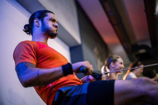  Low angle shot of a determined male athlete pulling handles on a rowing machine, highlighting upper body strength and core stability during a gym workout.