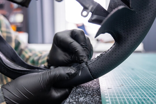 A seamstress in a workshop makes a new leather cover for a car steering wheel.