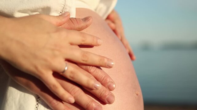 Close up of pregnant woman belly surrounded by the hands of future parents creating a tender family moment about pregnancy love anticipation and welcoming a new baby