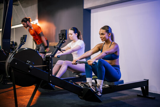 Wide shot of men and women lined up in a modern fitness studio, performing synchronous rowing exercises during a workout class.