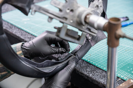 A seamstress in a workshop makes a new leather cover for a car steering wheel.