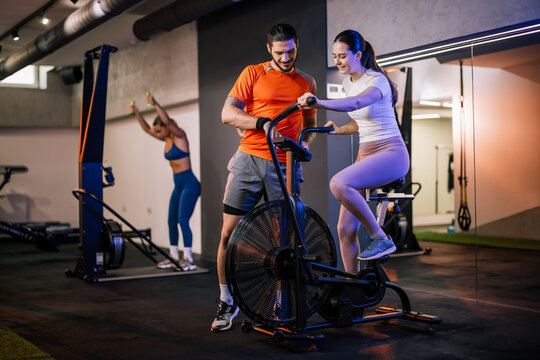  A male coach stands in front of a group of people on rowing machines, cheering them on and directing a high-intensity group class.