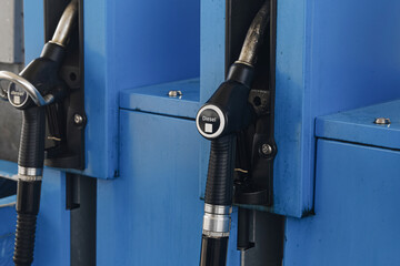 Diesel fuel nozzles at station. Black handles rest inside blue pumps. Metal spouts point upward. Diesel labels mark both dispensers. Fuel equipment fills background. Refueling hardware in closeup. © Paweł Michałowski