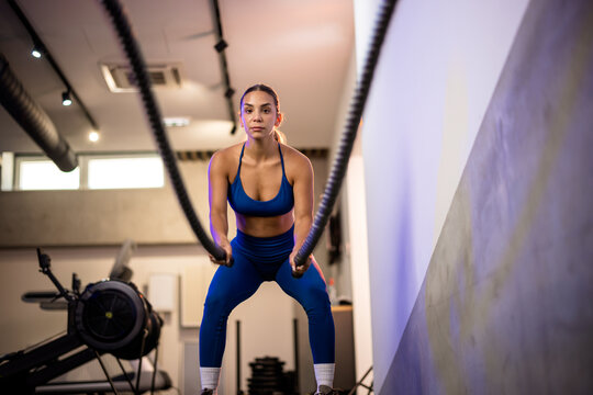 Symmetrical shot of a determined woman in blue activewear slamming battle ropes, creating clean visual waves that highlight functional core power.