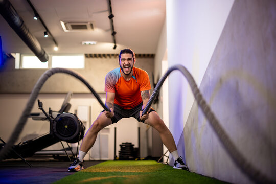 Wide angle shot of a determined fitness man finishing a gruelling battle ropes interval workout, showcasing peak physical performance and conditioning.