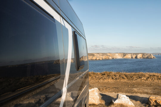 View of the Pen Hir cliffs reflecting on the side of a camper van parked on the rugged coastline in Camaret-sur-Mer, Bretagne, France.