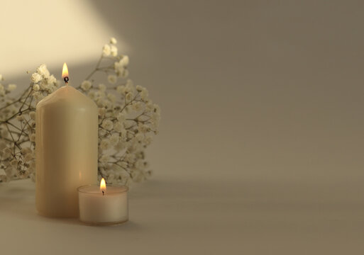 Soft focus blur Burning Candles with flower twig. Evening Light and shadow beige reflection background. Minimalist still life.